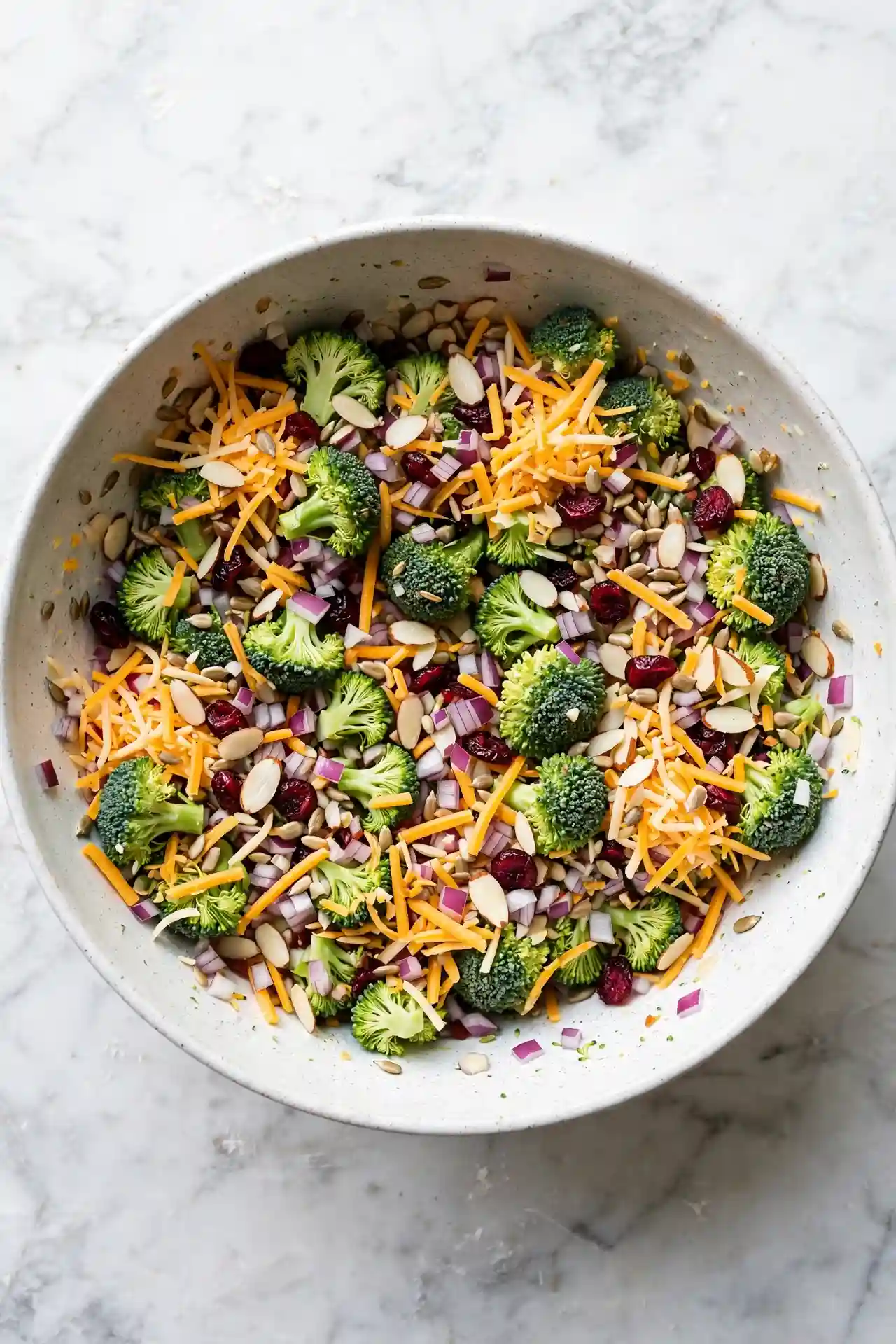 Broccoli florets, cheddar, red onion, sunflower seeds, almonds, and cranberries combined in a mixing bowl before dressing is added — step in making broccoli salad