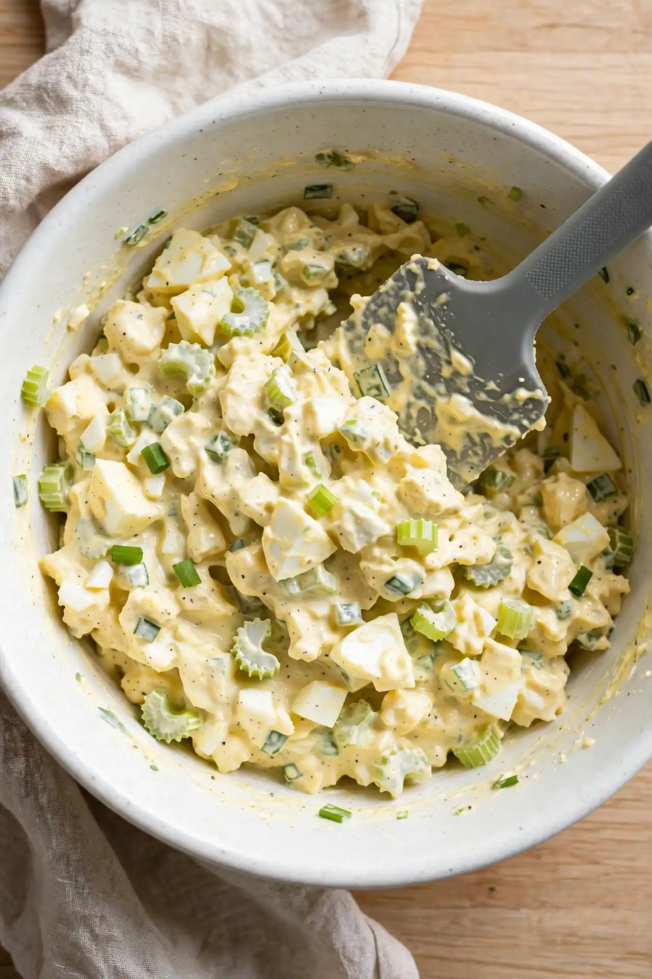Egg salad being folded together in a white bowl, final step in making this egg salad recipe